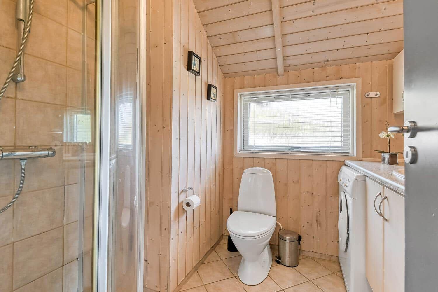 Bad mit Dusche, Toilette und Waschmaschine. Holzwandungen und Fenster mit Jalousie.