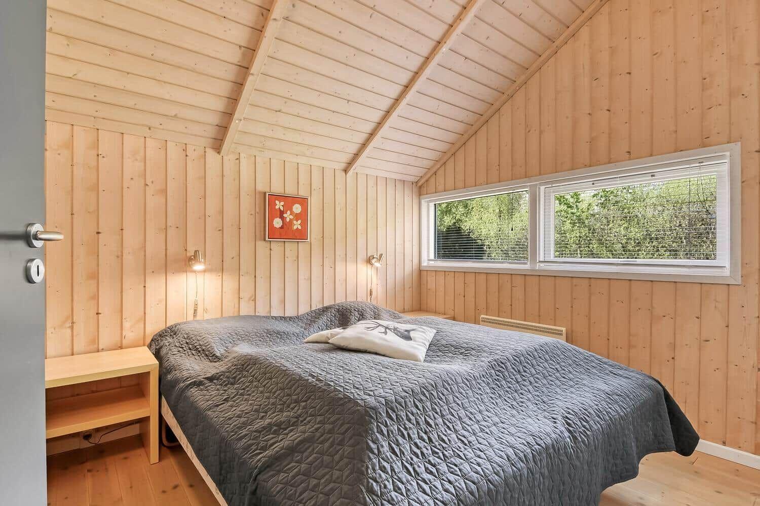 Schlafzimmer mit Holzwand, Bett und Fenster zum Blick auf Bäume.
