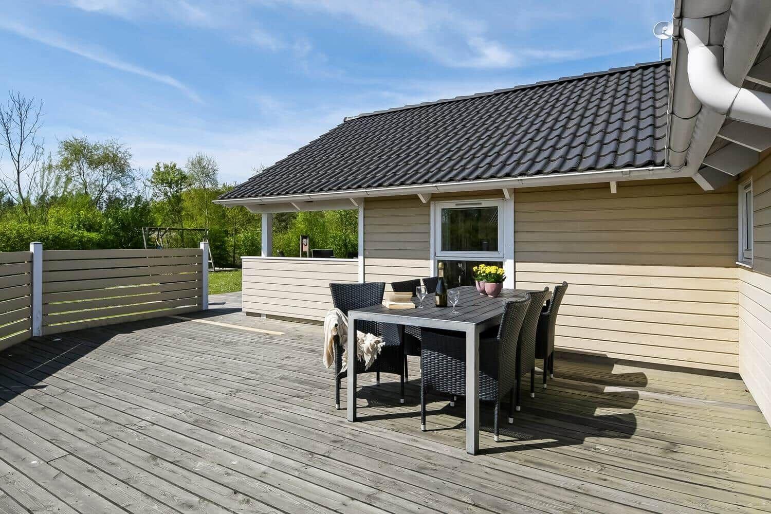 Terrasse mit Tisch und Stühlen vor einem Haus mit Holzfassade und Dach.