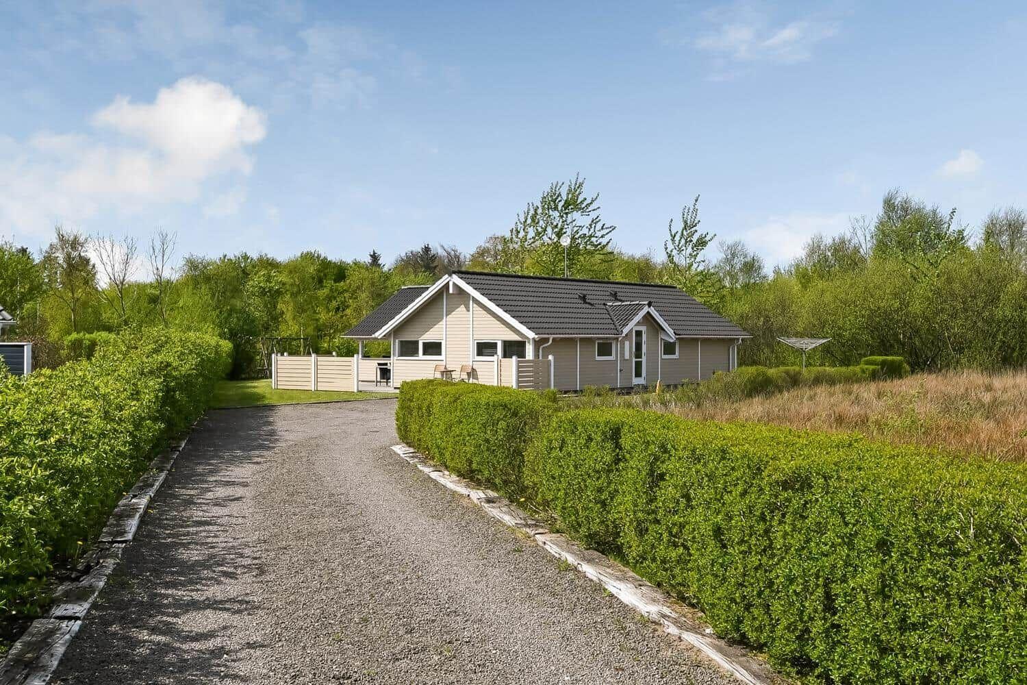 Ein Haus mit grauem Dach und Holzfassade steht hinter einem Kiesweg und grünen Hecken.