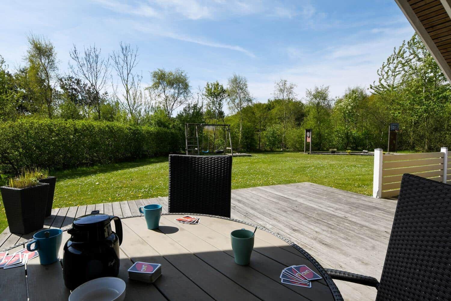 Terrasse mit Tisch, Stühlen und Blick auf den Garten mit Schaukel.