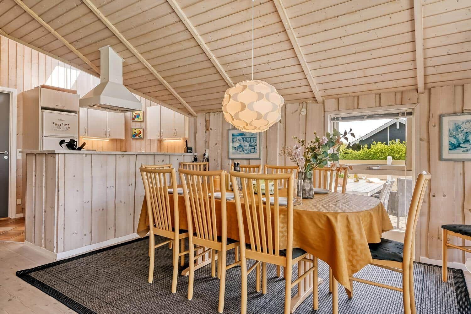 Essbereich mit Holztisch, Stühlen und Küchenzeile unter Holzdecke.