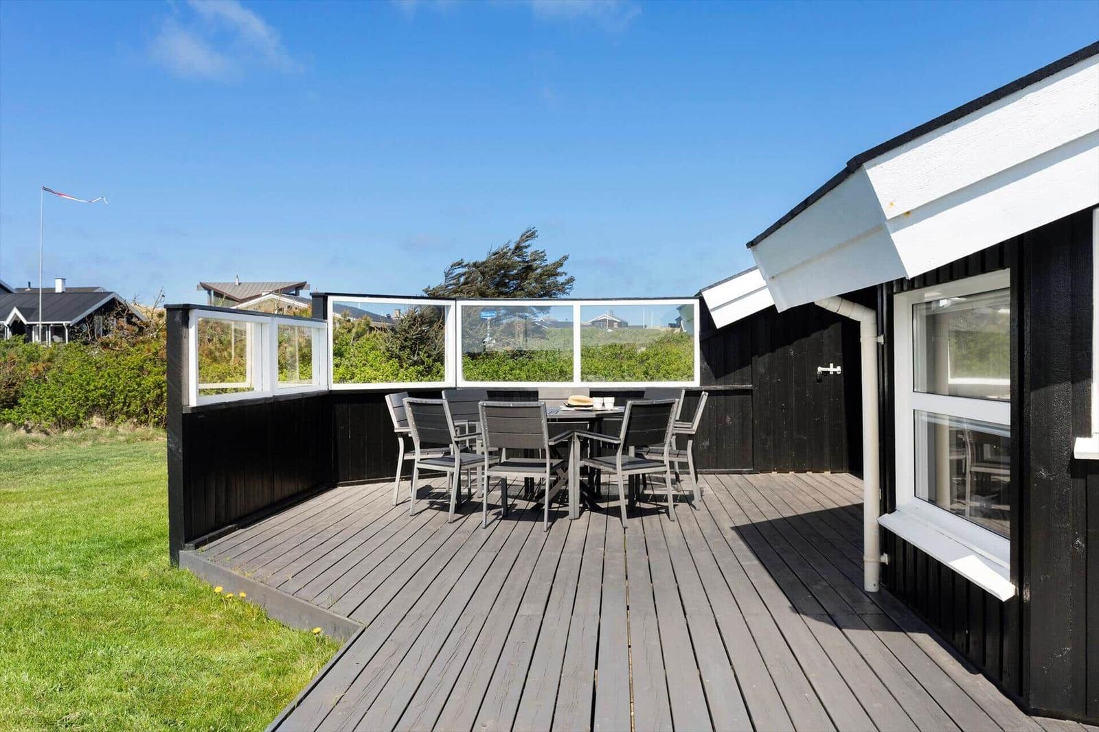 Terrasse mit Tisch und Stühlen, schwarze Holzwände und weißem Fensterrahmen.