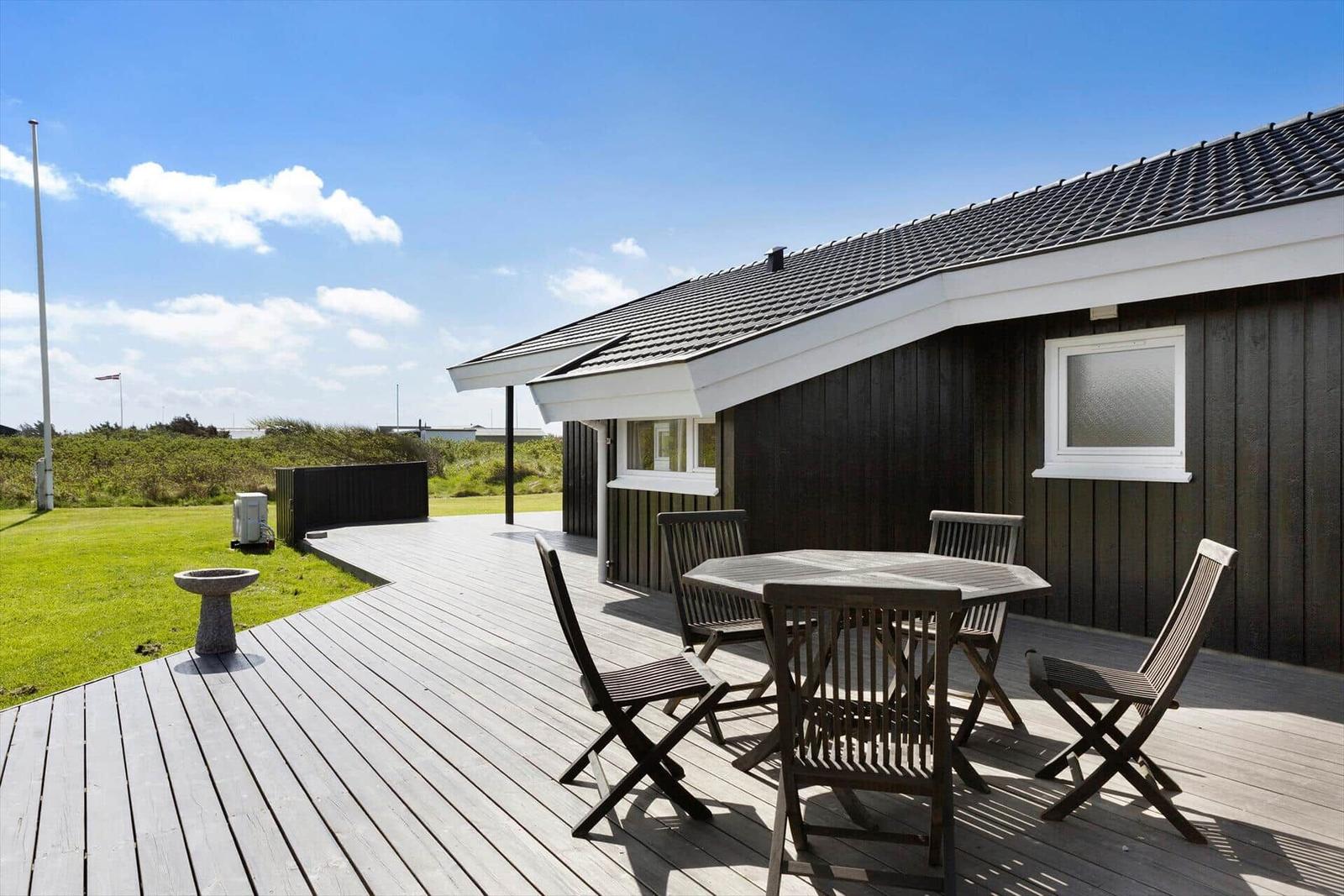 Terrasse mit Tisch und Stühlen neben einem Haus mit Holzfassade.