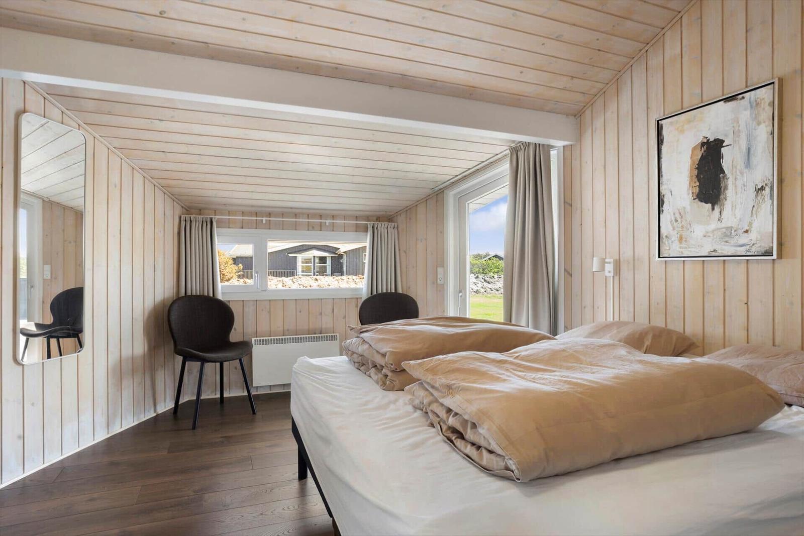 Schlafzimmer mit Holzwand, Bett, Fenster und Wandbild.