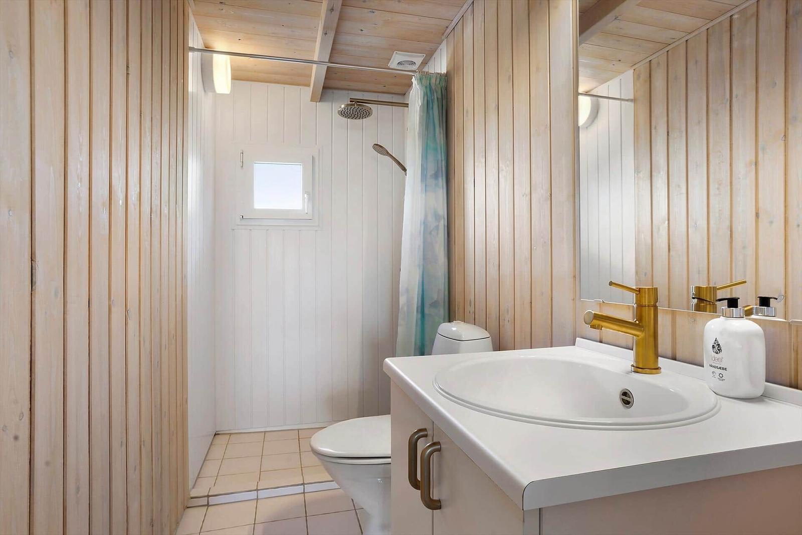 Bad mit Dusche, Toilette und Waschbecken mit goldenem Wasserhahn.