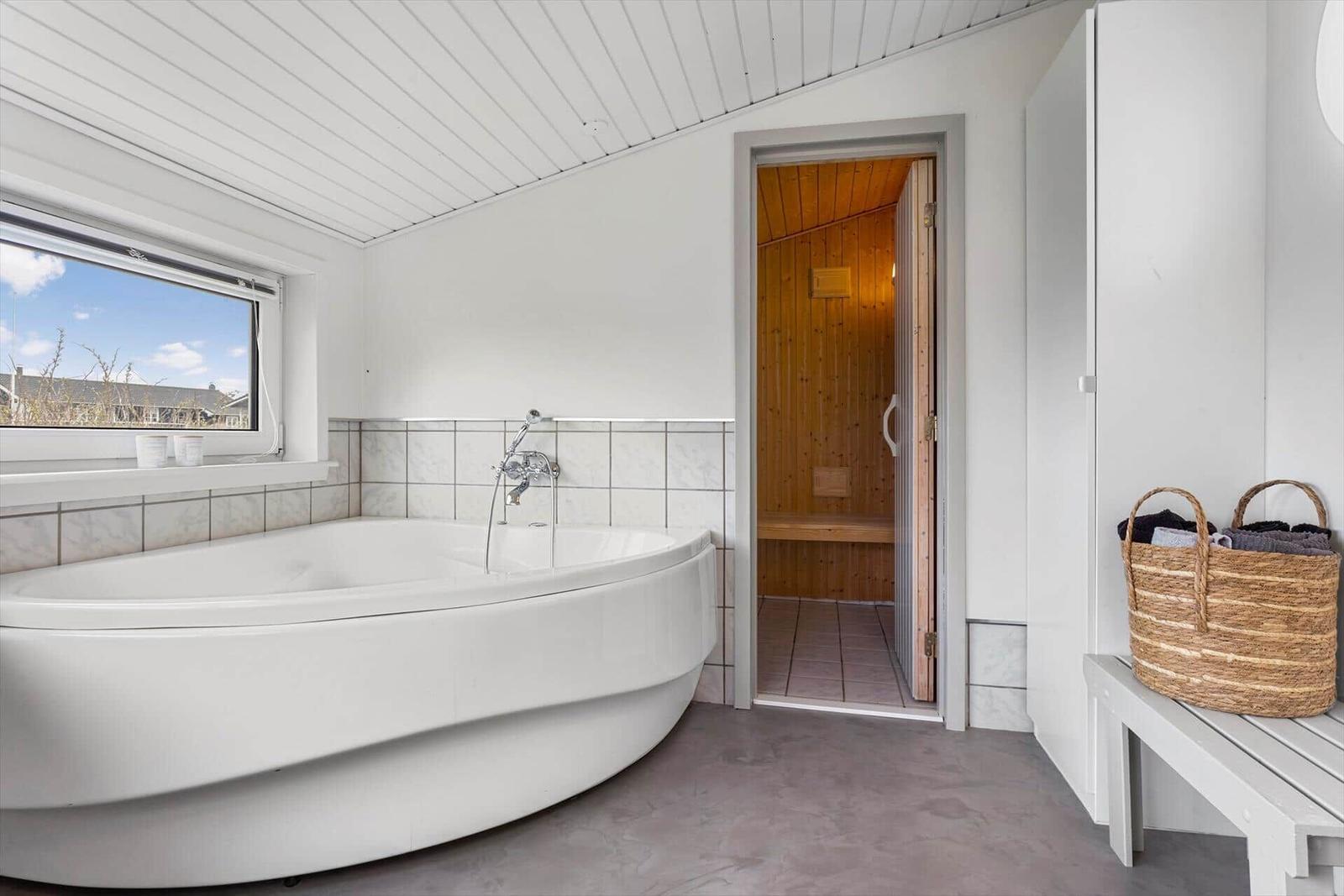 Bad mit Badewanne und Sauna im Hintergrund.