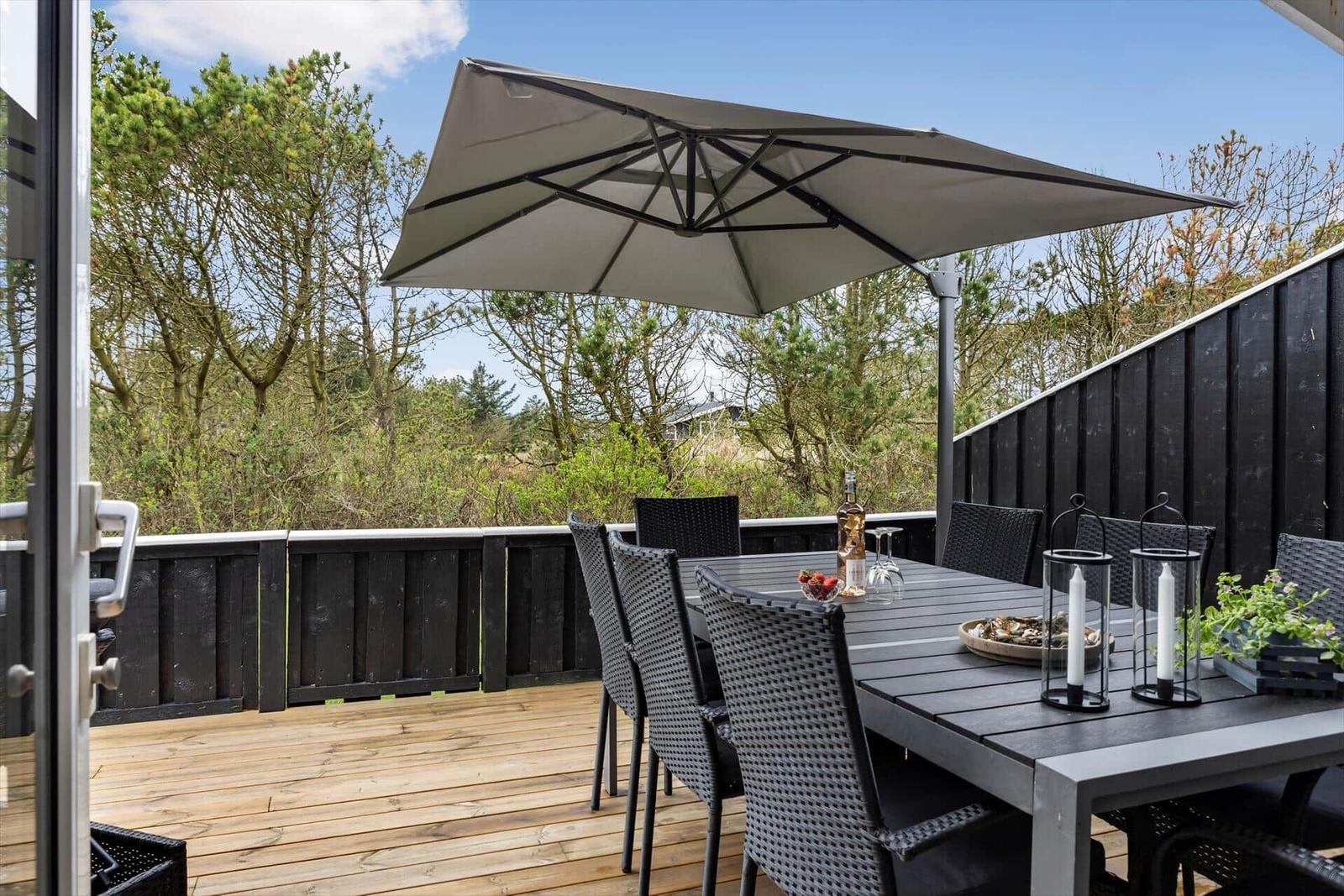 Terrasse mit Tisch, Stühlen und Sonnenschutz. Holzdecke und schwarze Umrandung.
