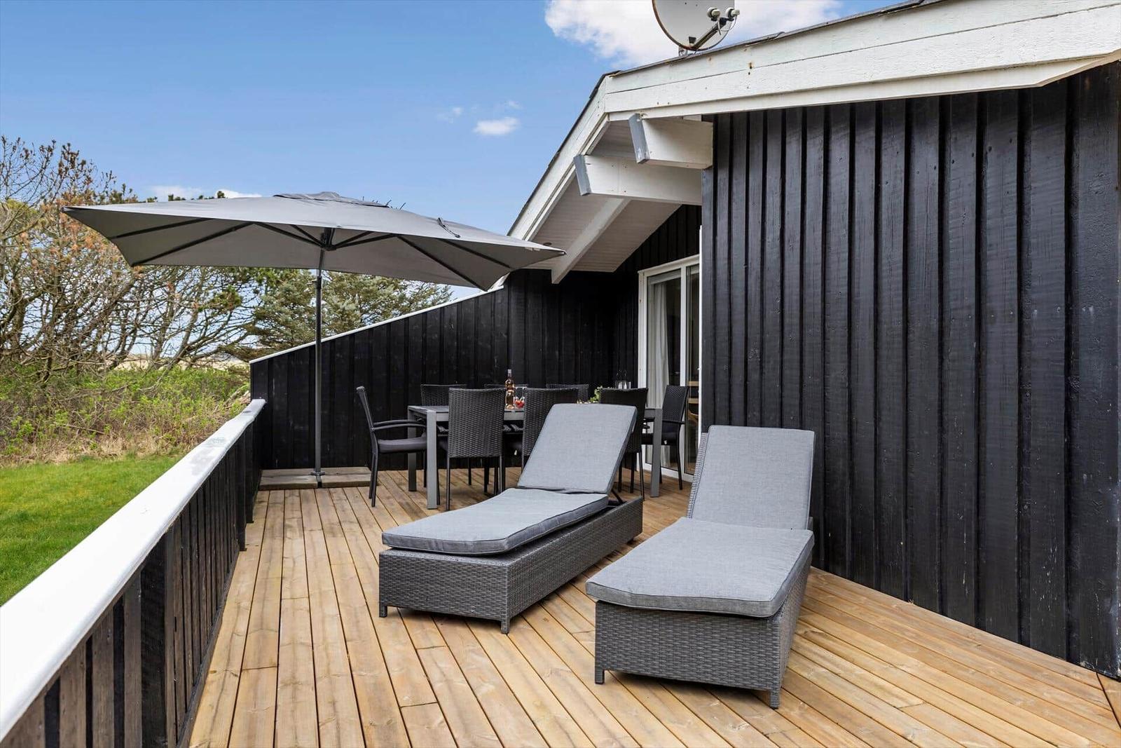 Terrasse mit Liegestühlen, Tisch und Sonnenschirm. Schwarze Holzwand und Holzdecke.