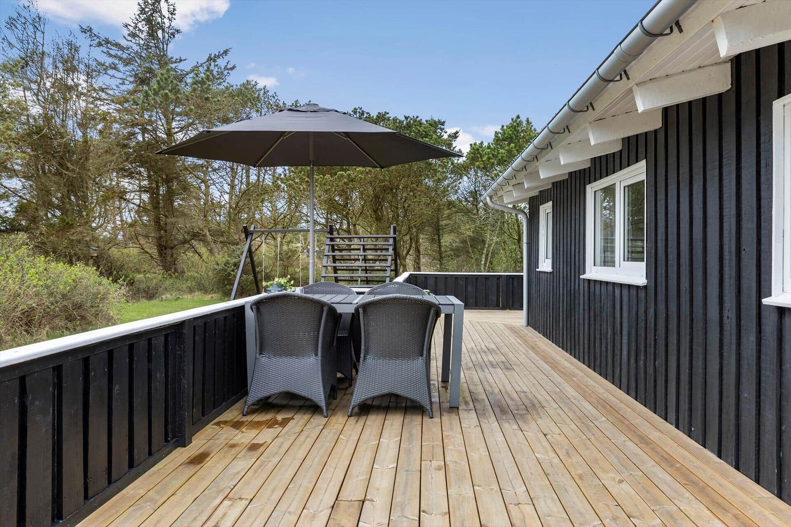 Terrasse mit Tisch, Stühlen und Sonnenschirm neben einem Haus mit schwarzer Fassade.