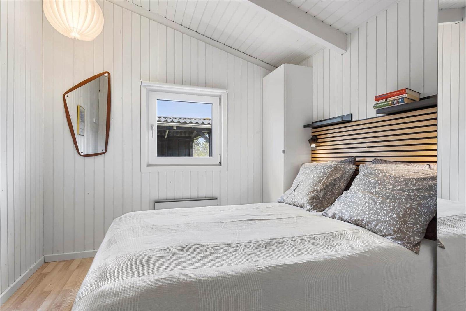 Schlafzimmer mit Bett, Fenster und Spiegel an der Wand.