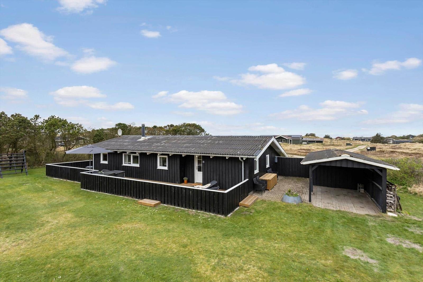 Schwarzes Holzhaus mit Terrasse und Carport auf grünem Grundstück.