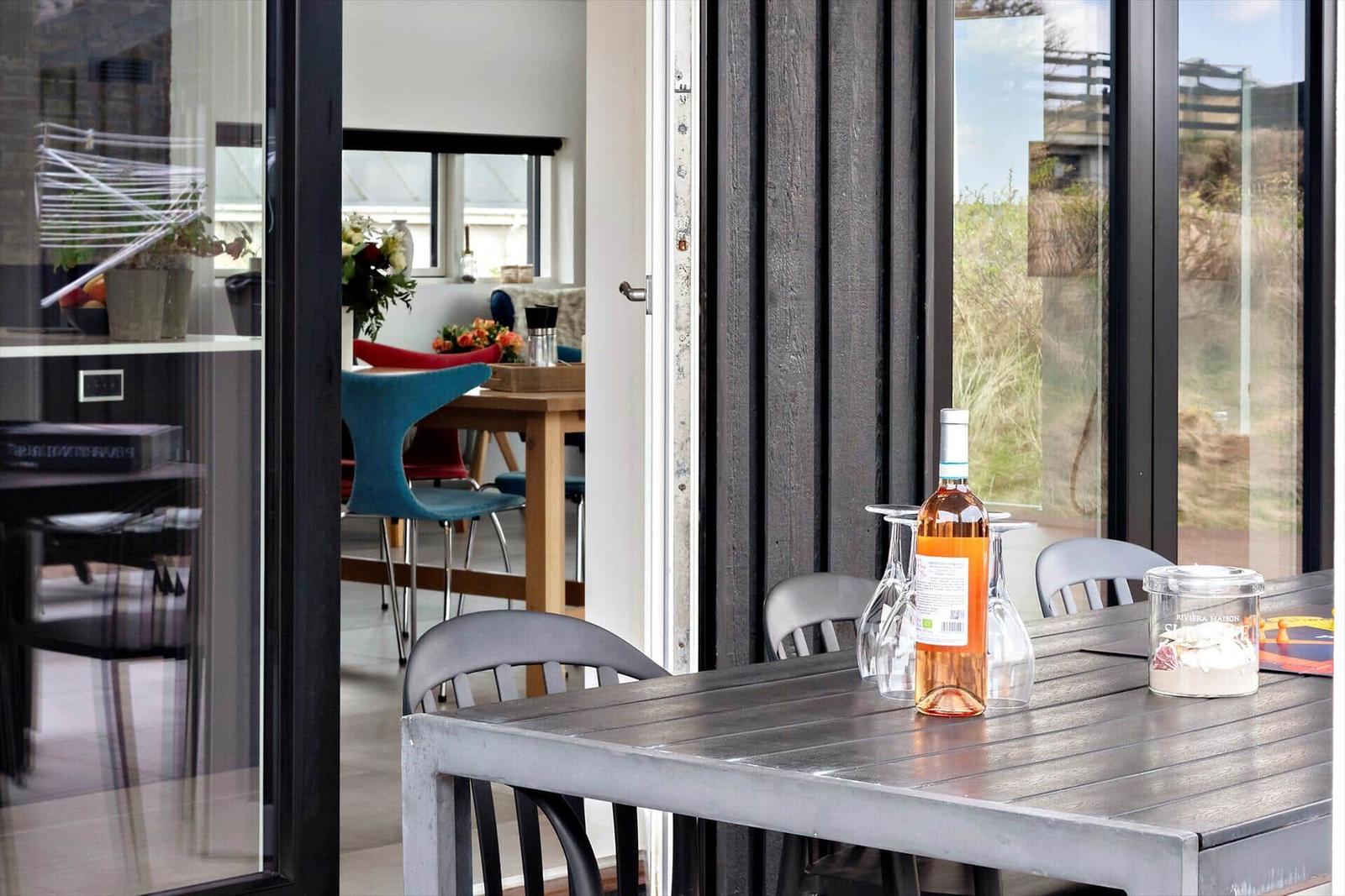 Terrasse mit Tisch, Stühlen und Flasche Wein. Durchgang ins Innere mit Essbereich.