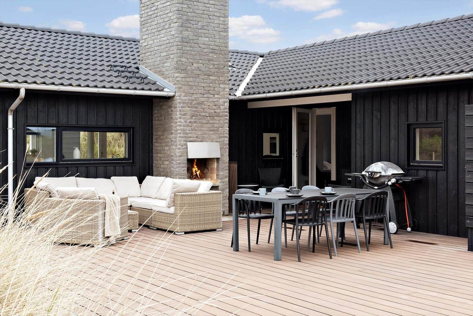 Terrasse mit Sitzgruppe, Esstisch und Grill. Außenkamin mit brennendem Feuer.