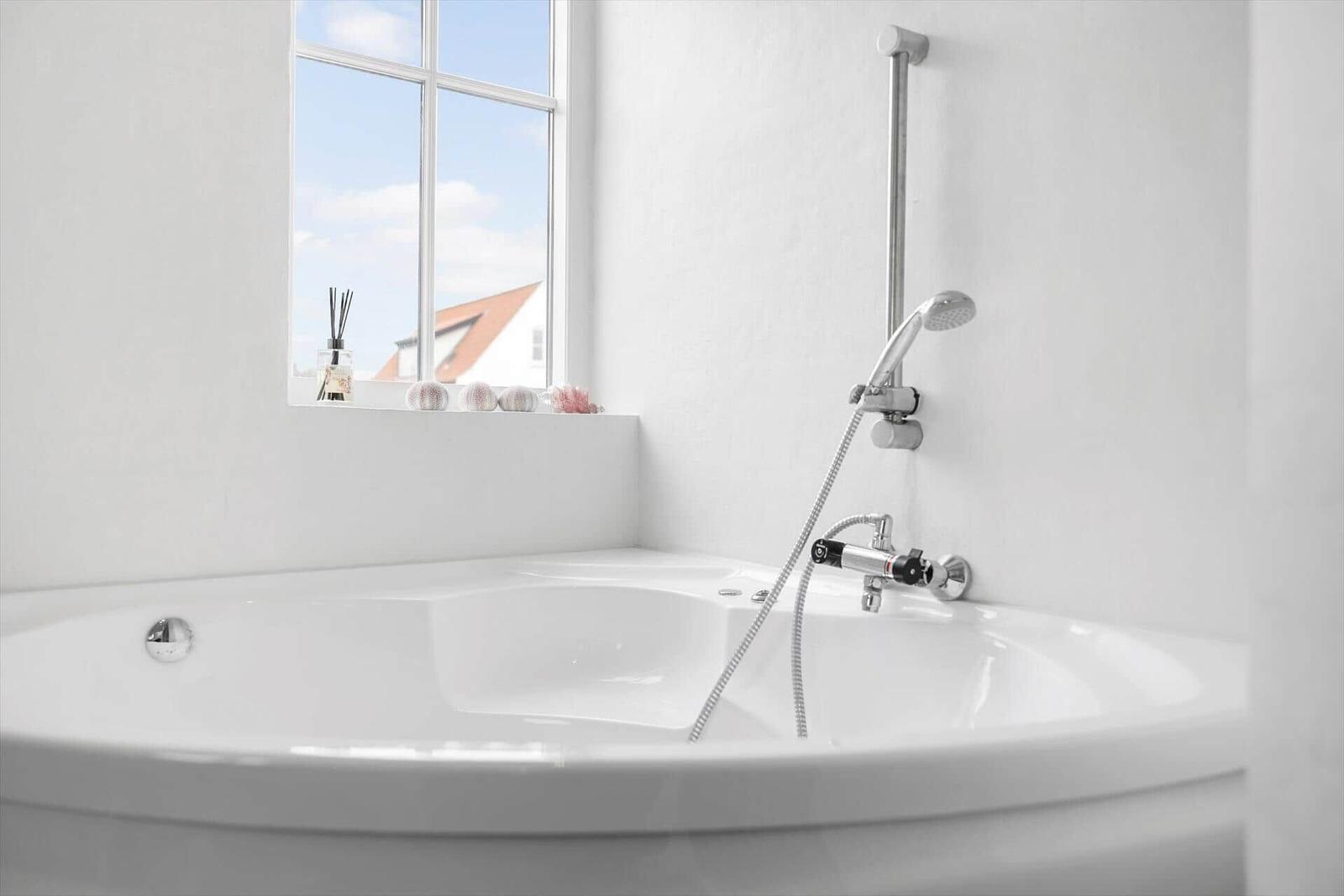 Eine weiße Badewanne mit Duschkopf und Fensterblick auf Dach