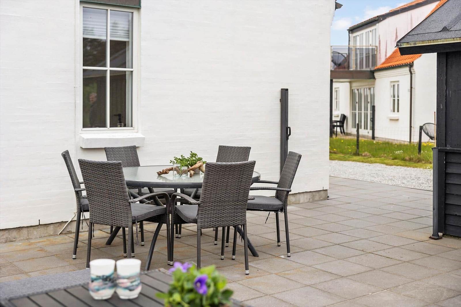 Terrasse mit Tisch und sechs Stühlen vor weißer Hauswand.