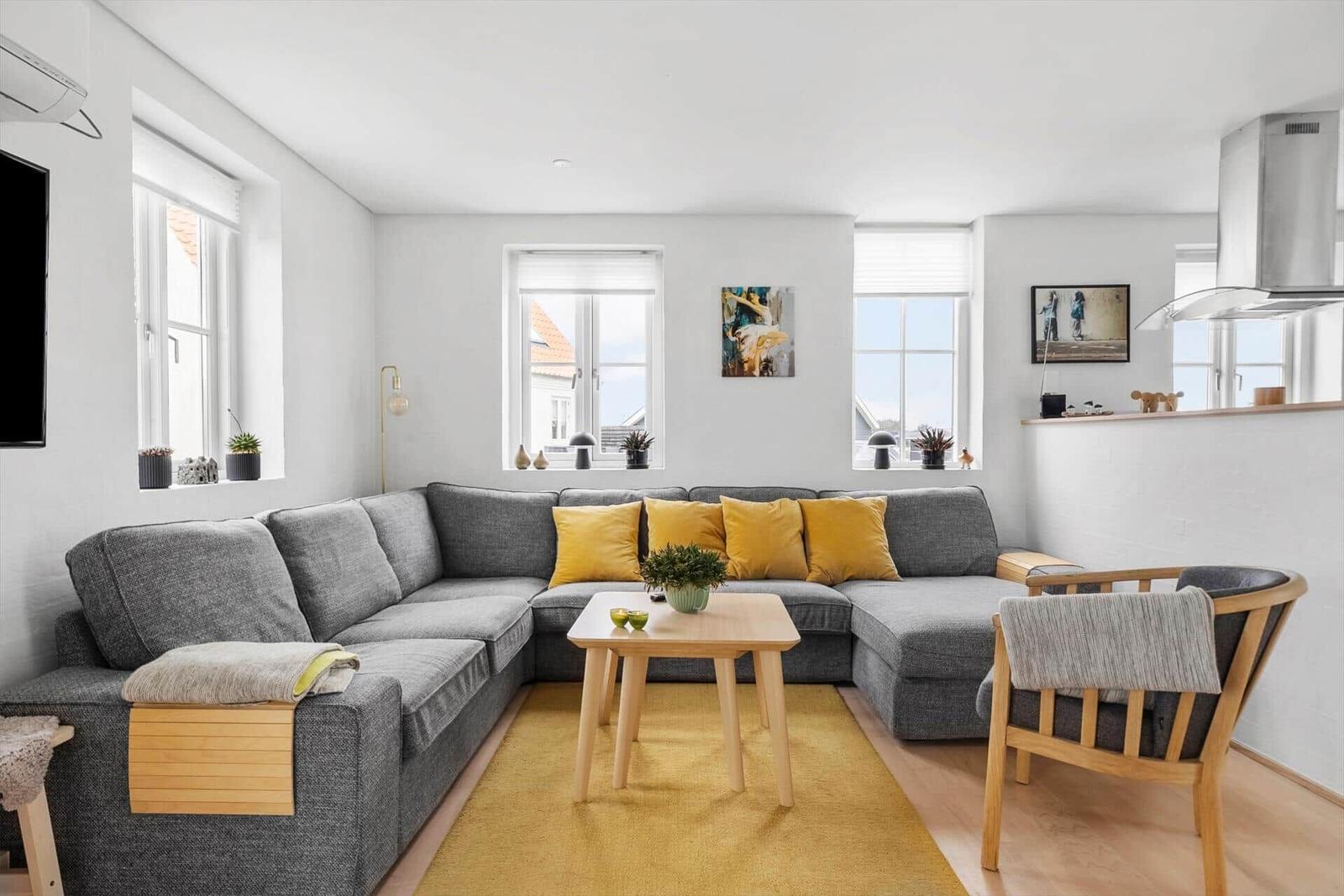 Ein Wohnzimmer mit grauem Sofa, gelbem Teppich und Holztisch.