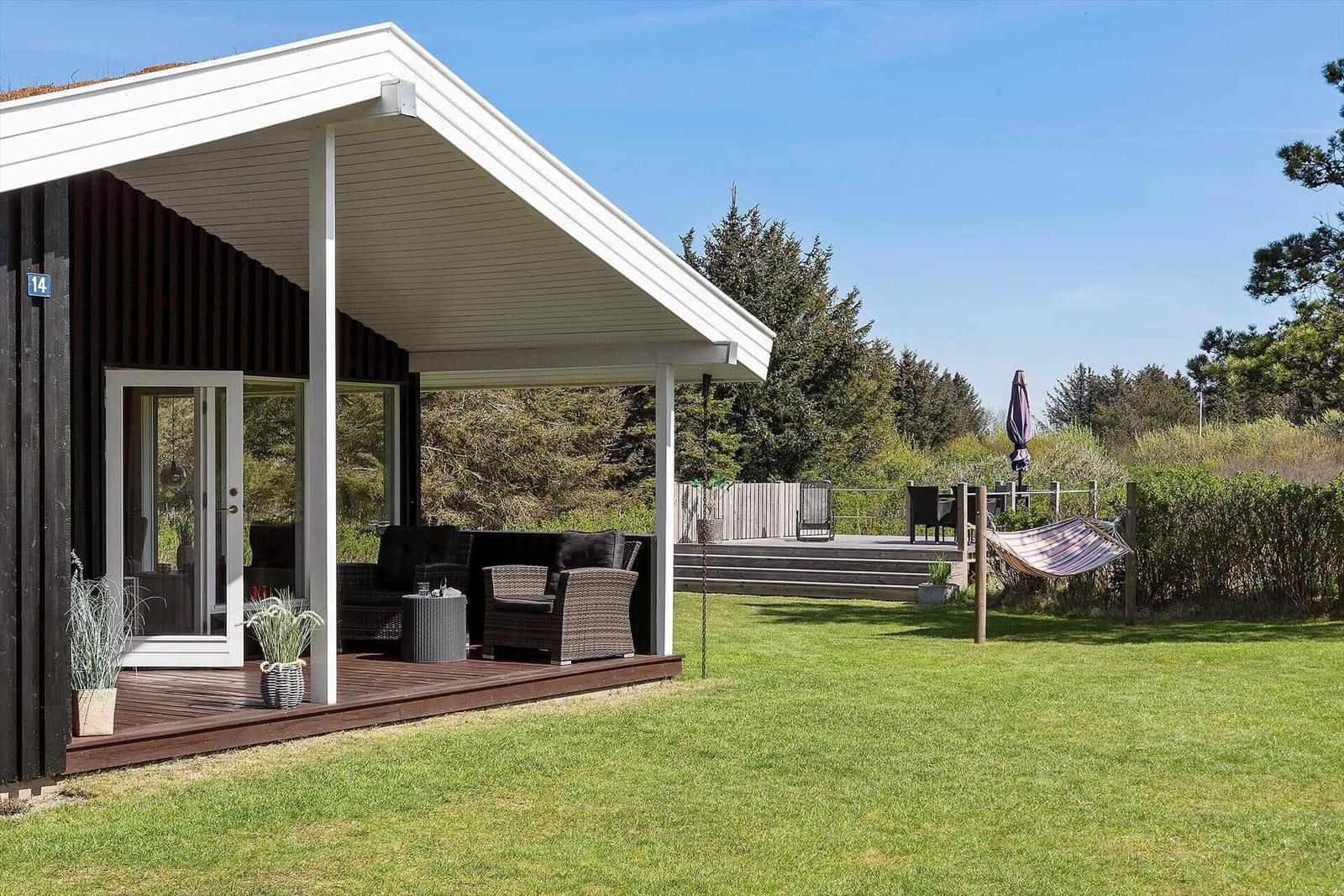 Haus mit Terrasse, Garten und Hängematten. Holzterrasse mit Sitzgelegenheiten.