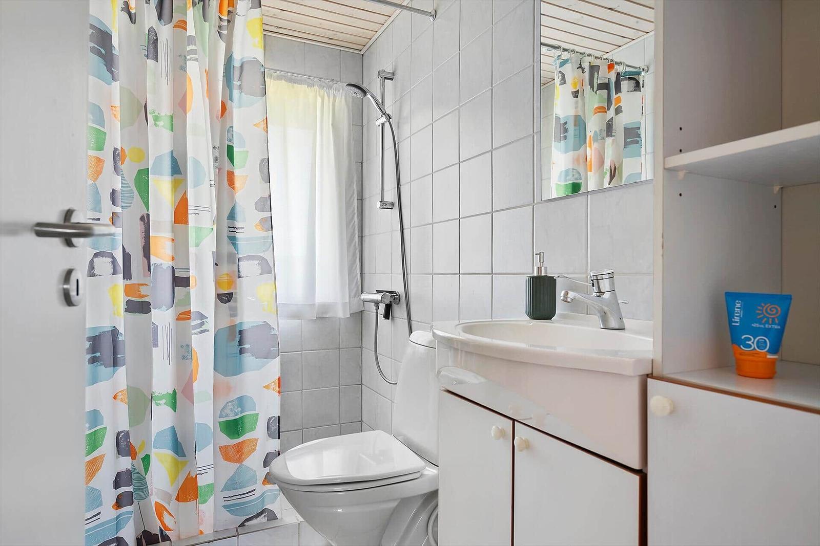 Badezimmer mit Dusche, Waschbecken und Toilette. Farbiger Duschvorhang und Spiegel.