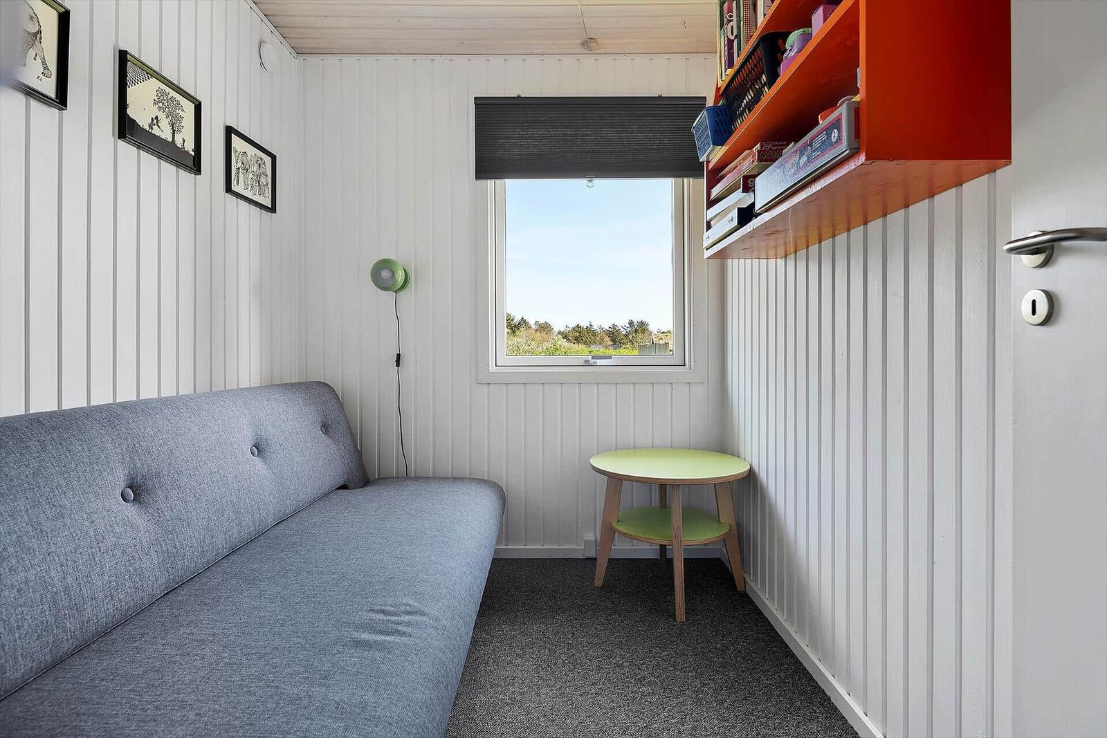 Ein Raum mit Sofa, Tisch und Fenster. Wandregal und Bilder an der Wand.