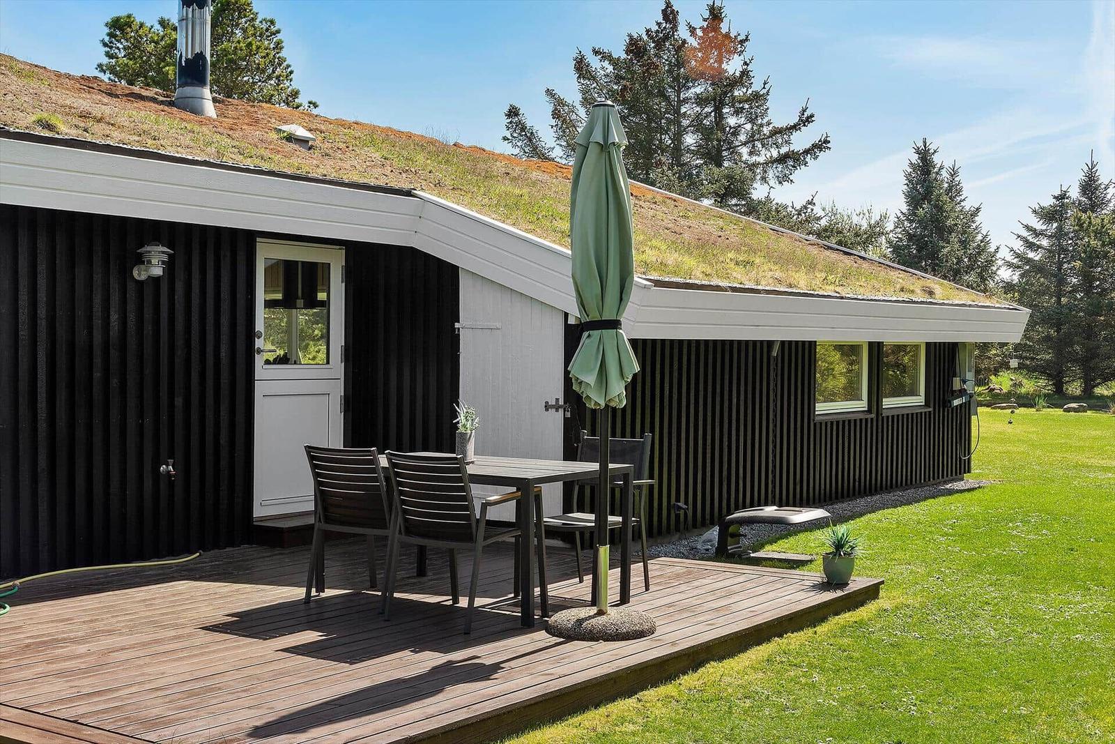 Haus mit Grasdach, Terrasse mit Tisch, Stühlen und Sonnenschirm.