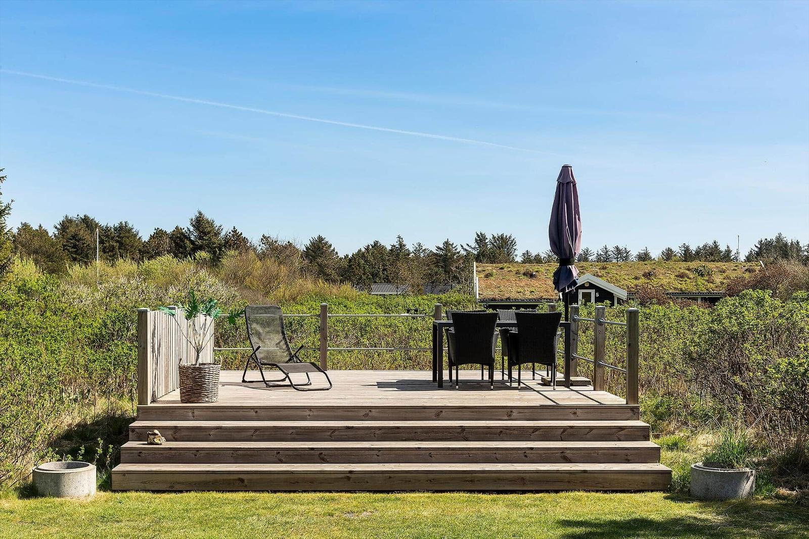 Terrasse mit Liegestuhl, Tisch und Stühlen. Blick auf grüne Landschaft und Himmel.
