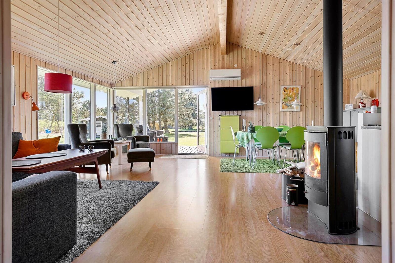 Wohn- und Essbereich mit Kamin, Holzdecke und großem Fensterblick auf Garten.