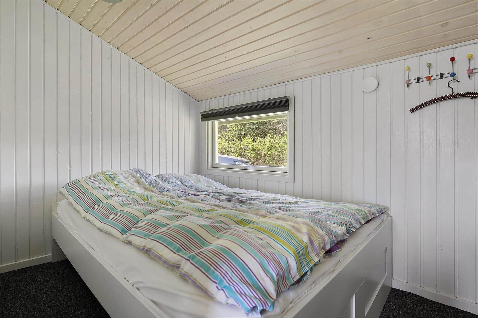 Schlafzimmer mit Bett, Fenster und Kleiderhaken an der Wand.