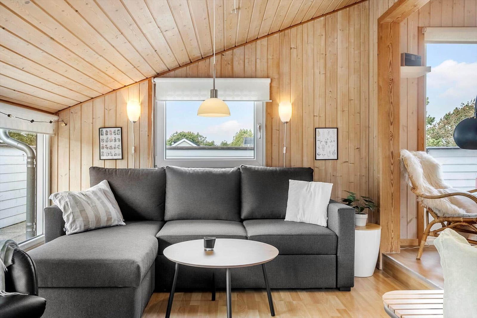Wohnzimmer mit grauem Sofa, runden Tisch und Holzwandverkleidung.