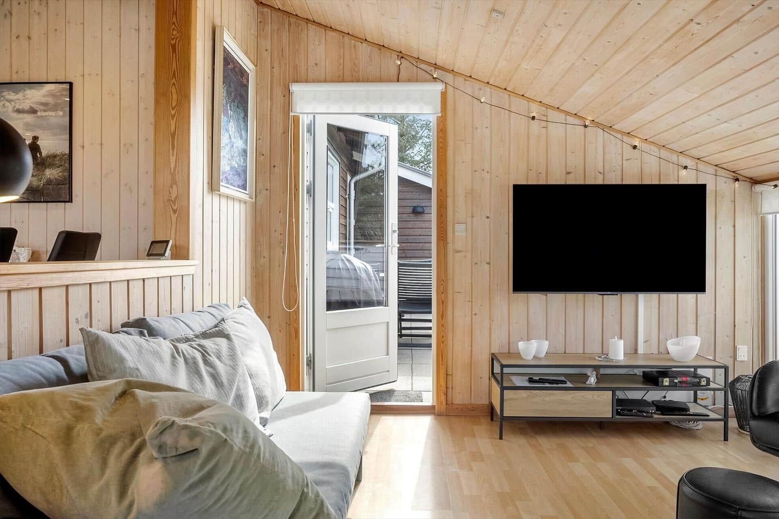 Wohnzimmer mit Sofa, Fernseher und Tür zum Außenbereich.