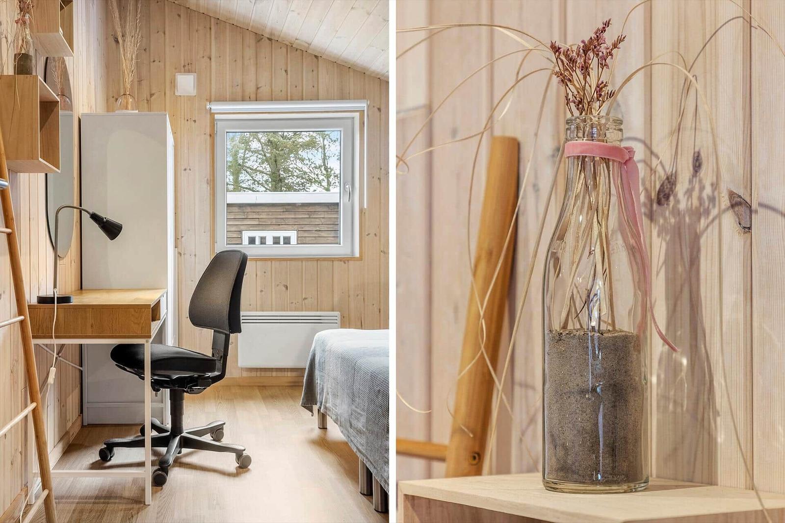 Schlafzimmer mit Schreibtisch, Bett und Fenster. Dekorative Glasvase mit Sand und getrockneten Pflanzen.