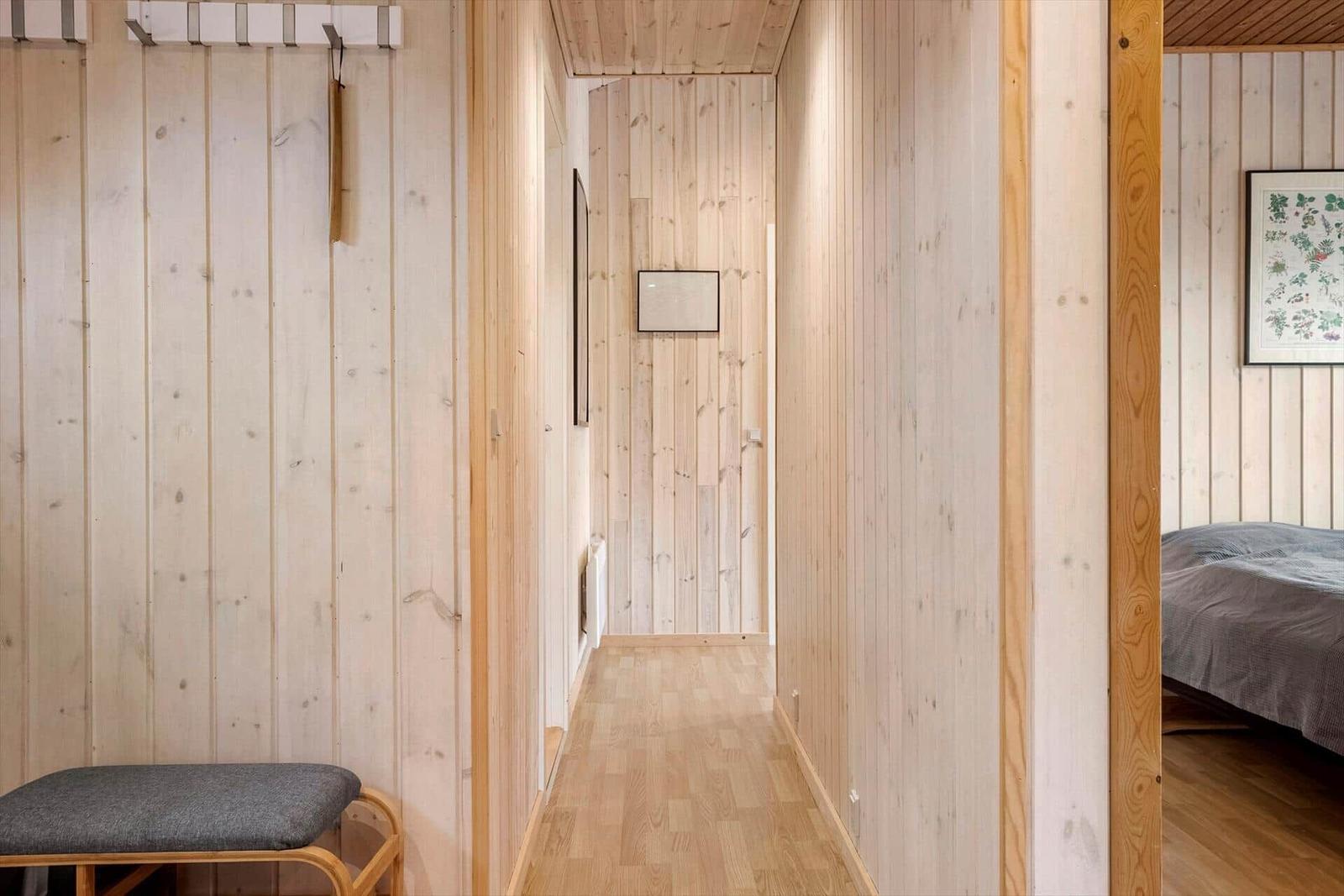 Flur mit Holzwandverkleidung, Sitzbank und Blick in Schlafzimmer mit Bett.