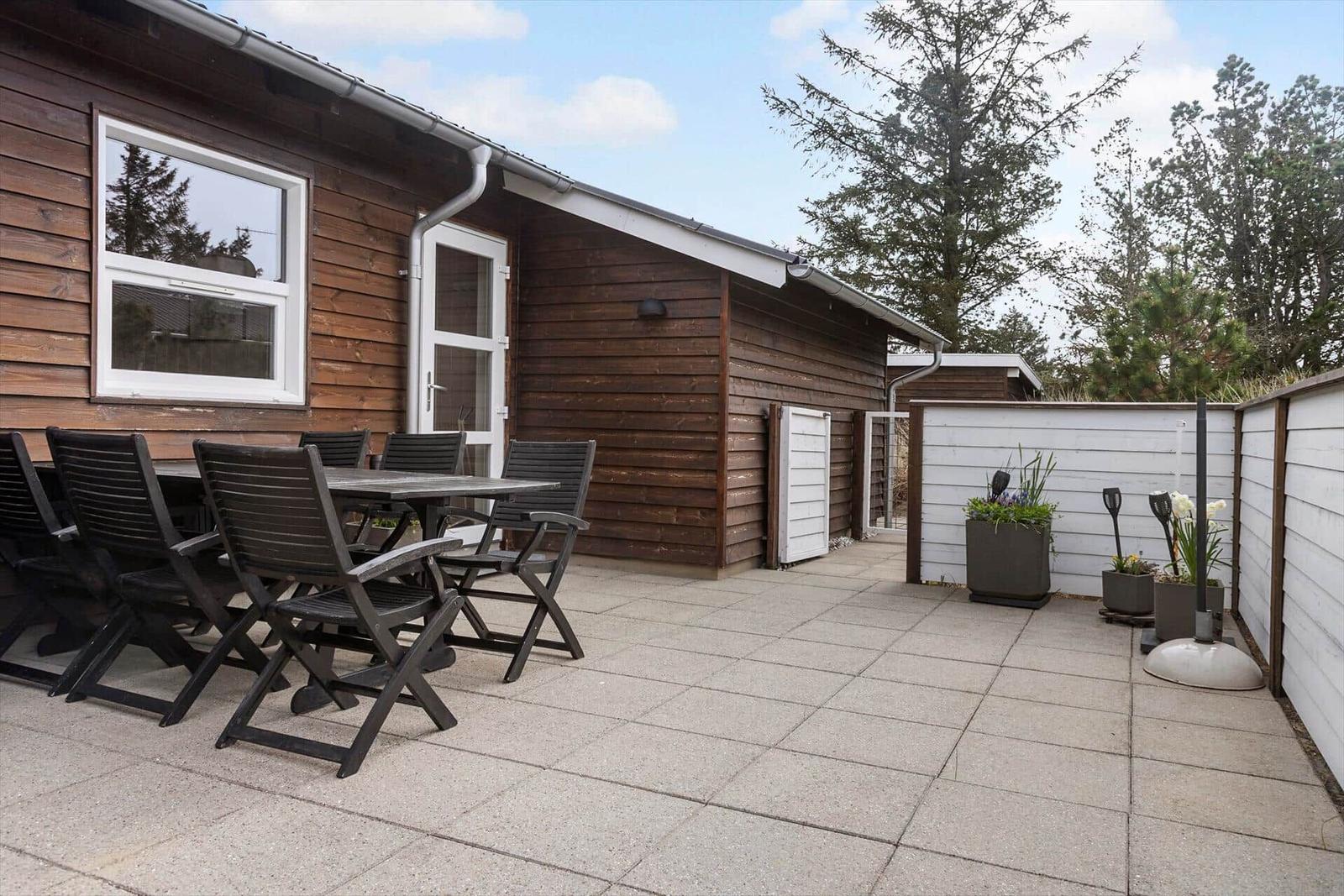 Terrasse mit Tisch und Stühlen vor Holzhaus mit weißen Fenstern und Tür.