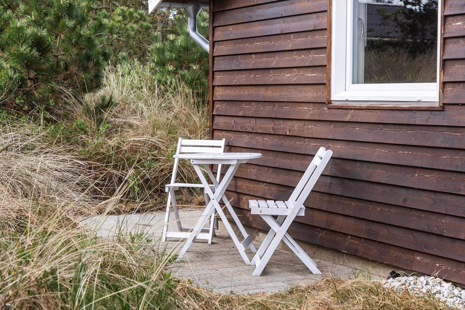 Weiße Tisch- und Stühle auf Terrasse neben Holzhaus mit Fenster