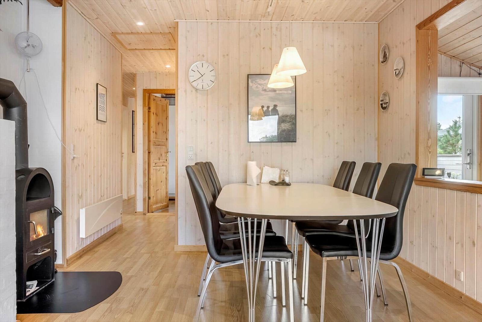 Esszimmer mit Tisch, Stühlen und Kaminofen. Holzwände und Boden.
