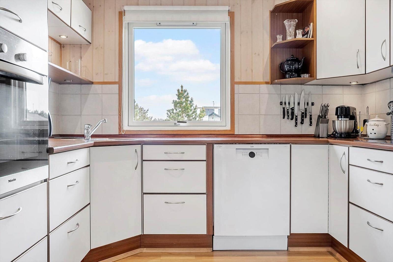 Küche mit weißen Schränken, Holzoberfläche und Fenster mit Blick auf Bäume.
