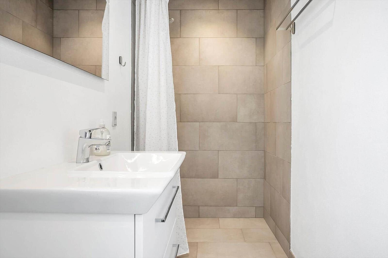 Badezimmer mit Waschbecken, Spiegel und Dusche mit Duschvorhang.