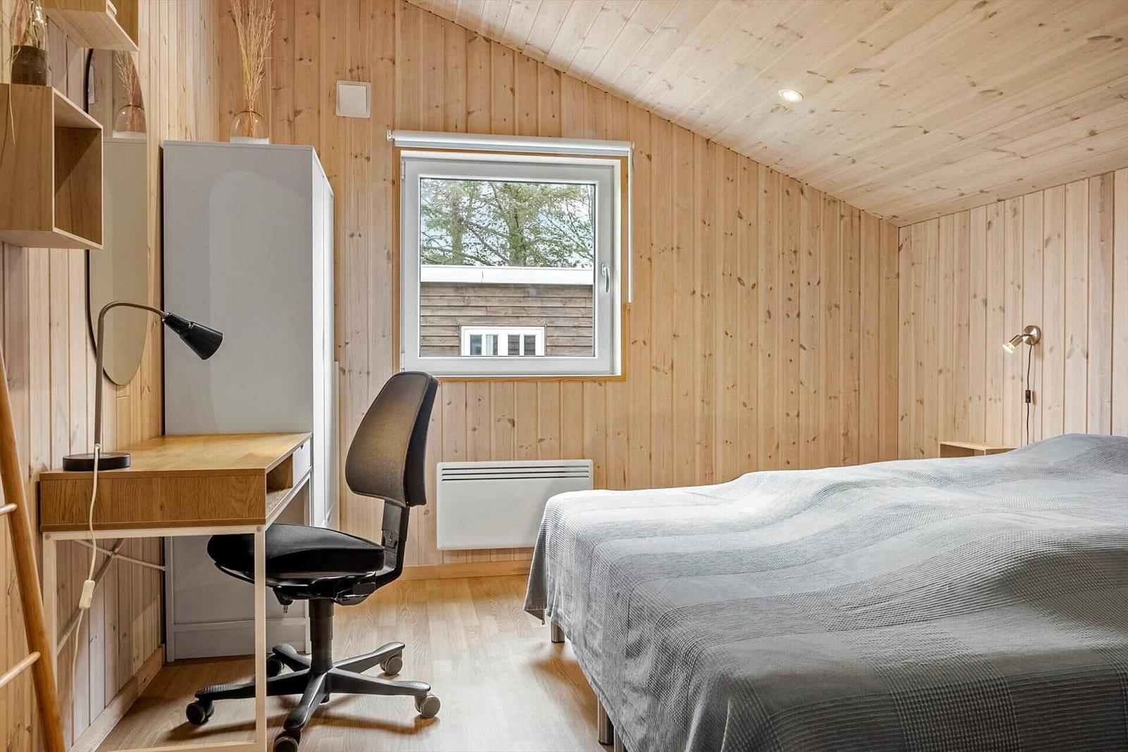 Schlafzimmer mit Bett, Schreibtisch und Fenster. Holzwände und -decke.