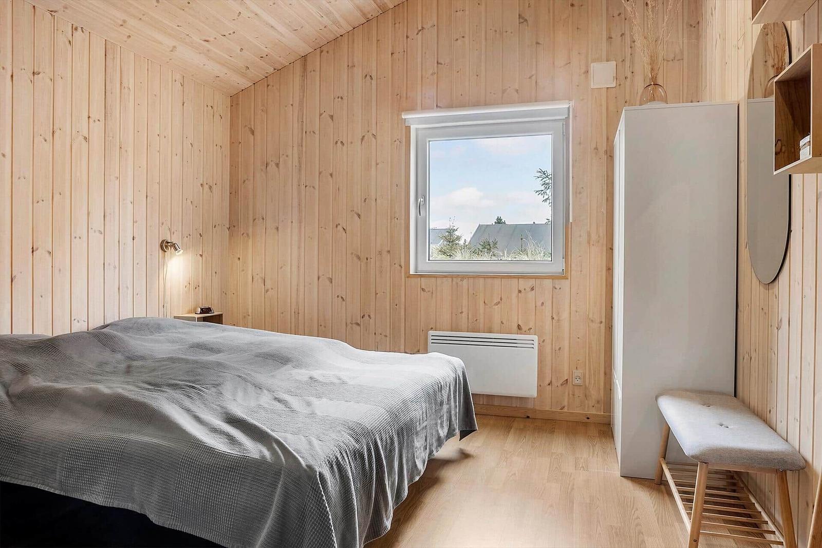 Schlafzimmer mit Holzwand, Bett, Fenster und Kleiderschrank.