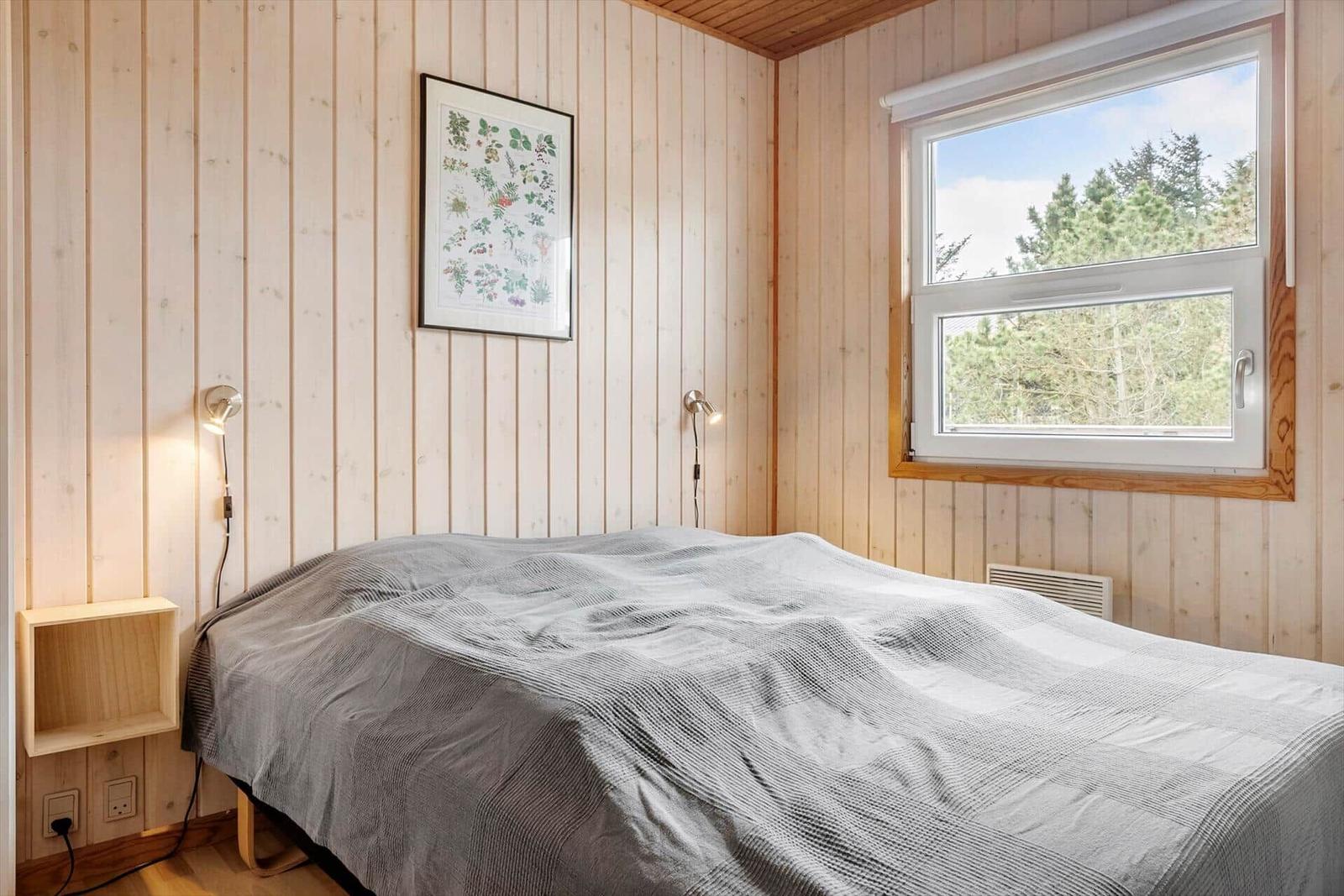 Schlafzimmer mit Bett, Fenster und Holzwandverkleidung.