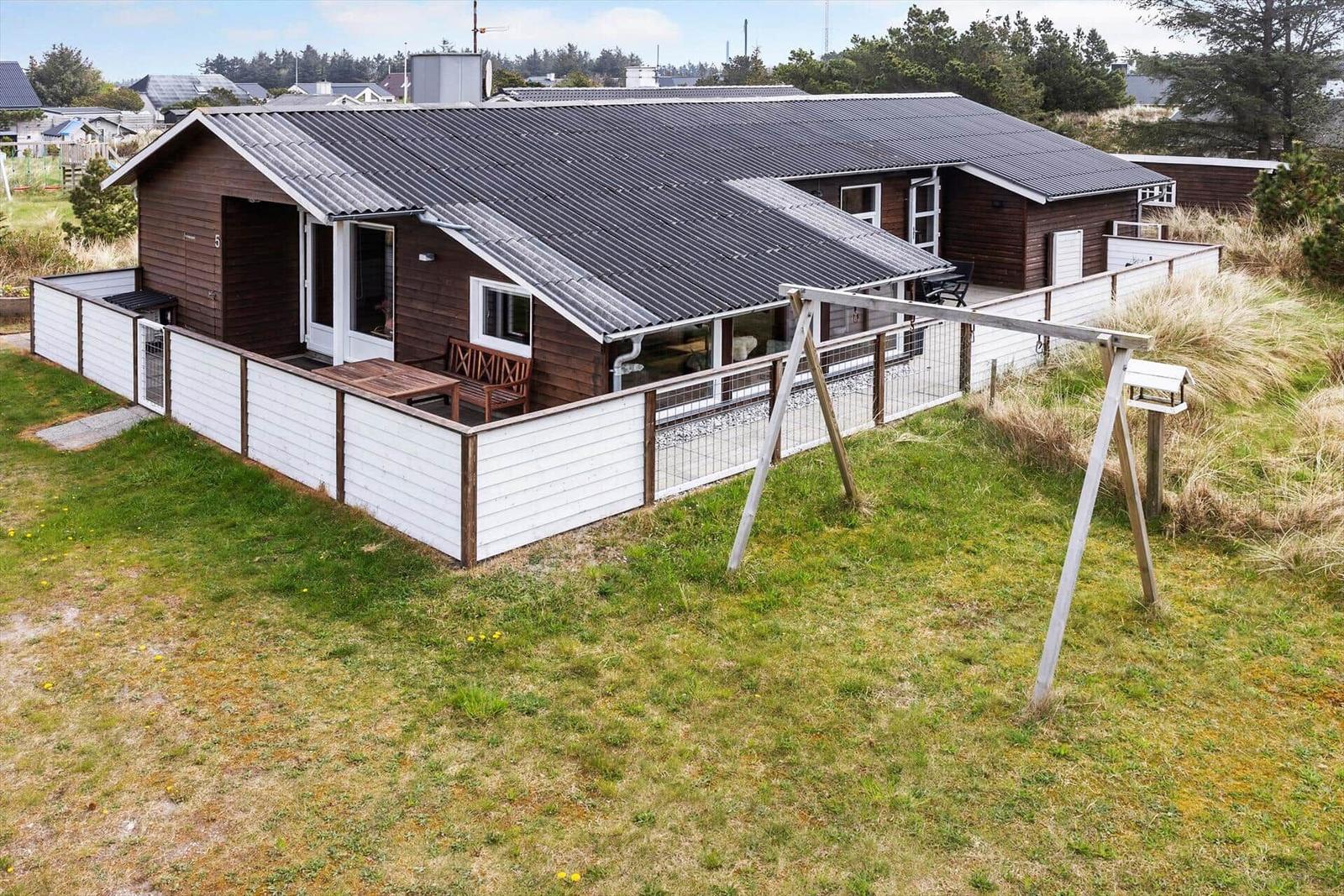 Holzhäuschen mit Terrasse und Garten. Holzveranda mit Sitzgelegenheit. Weiße Umzäunung und Schaukel.