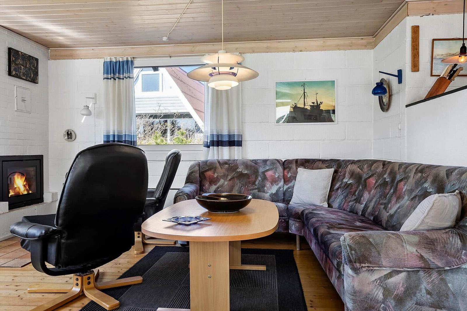Wohnzimmer mit Sofa, Esstisch und Kaminofen. Holzdecke und weiße Wände.