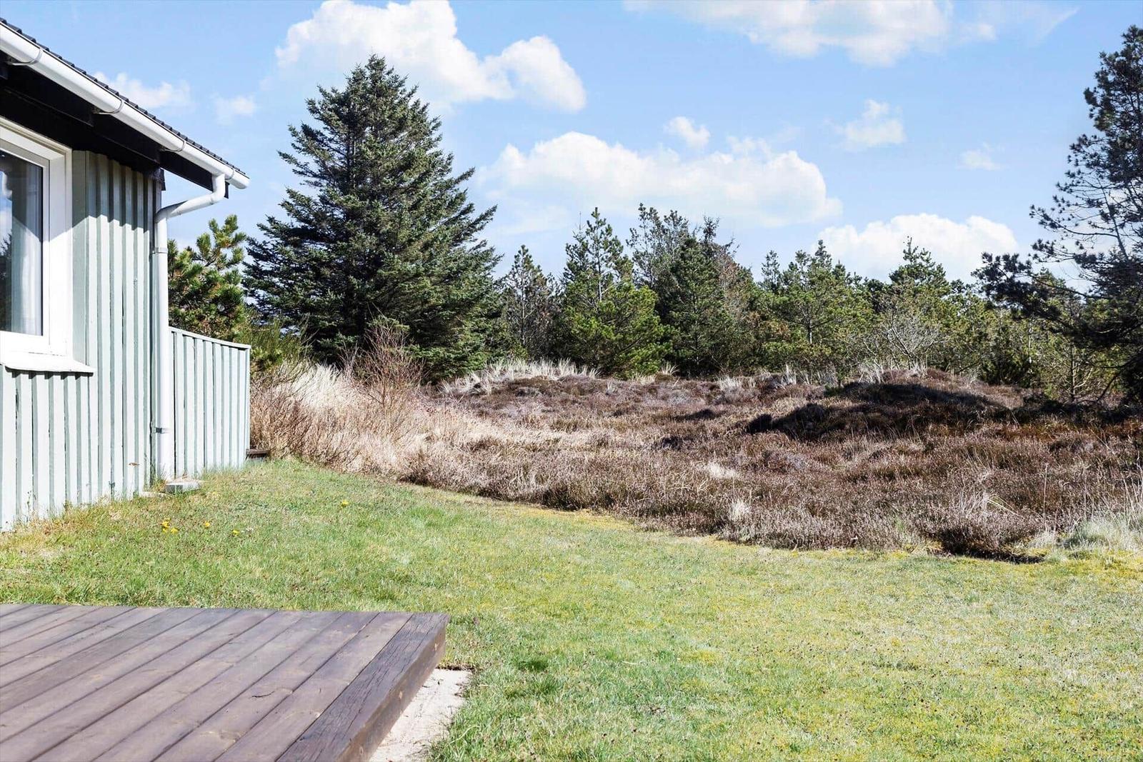 Haus mit Holzterrasse, Grasfläche und Wald im Hintergrund.