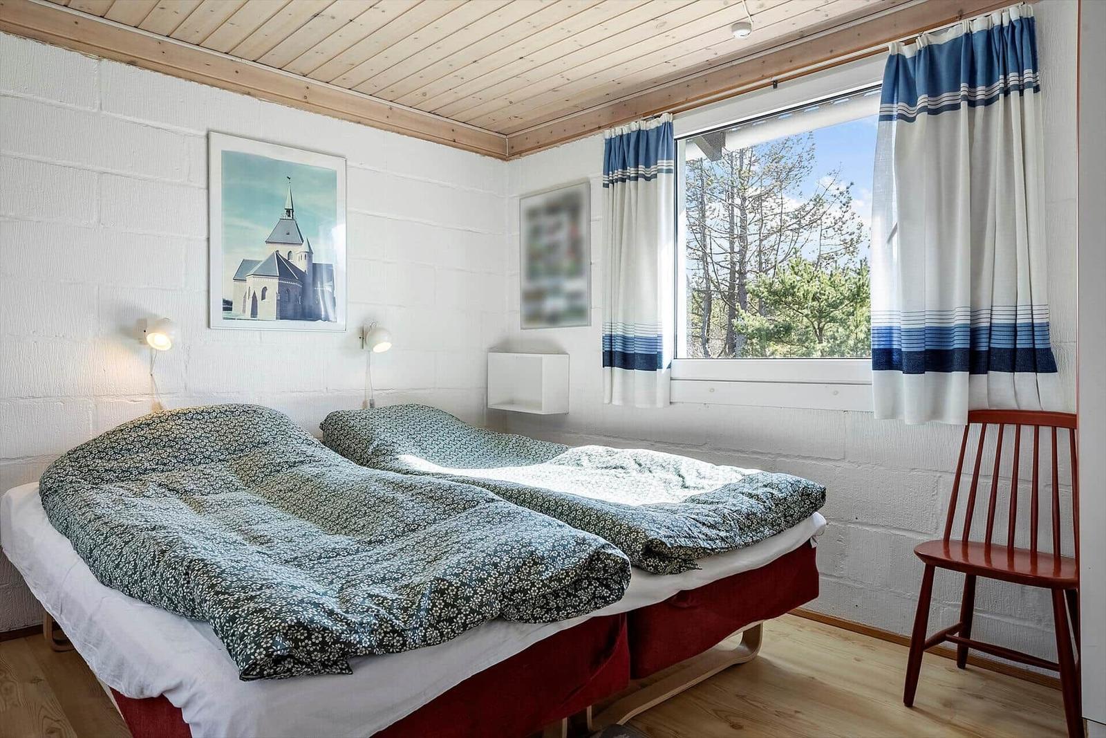 Zwei Betten mit gemusterten Bettdecken, Fenster mit Vorhängen und Stuhl.