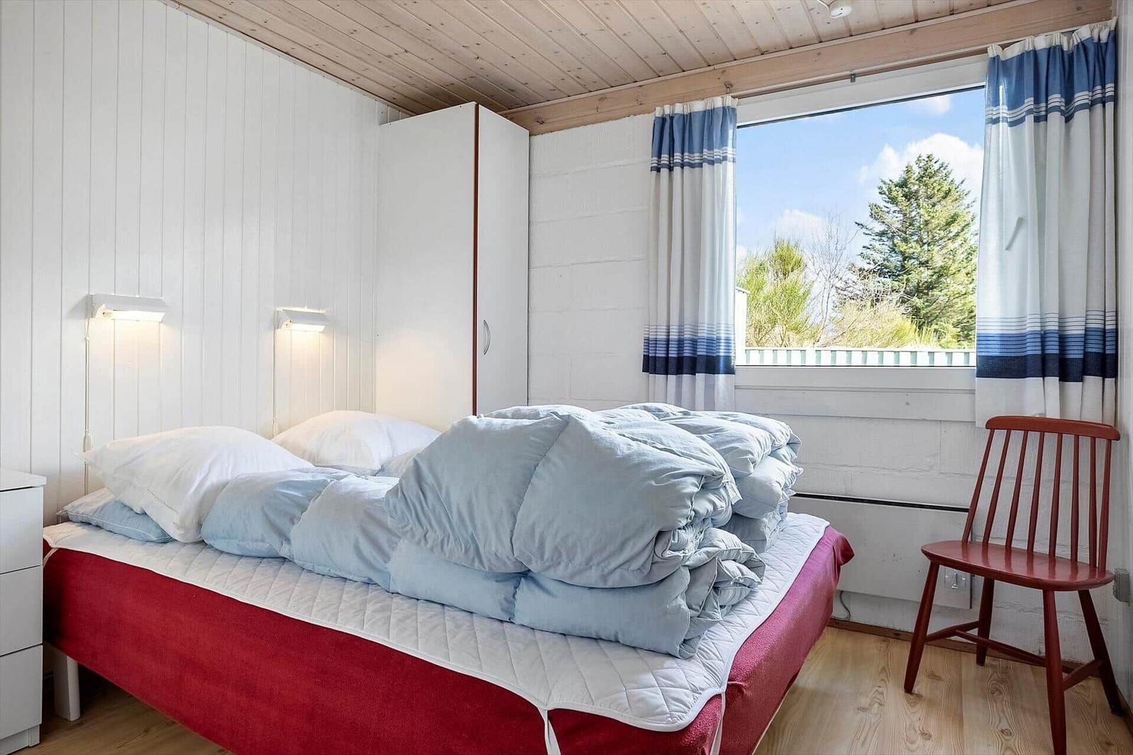 Schlafzimmer mit Bett, Kleiderschrank und Fenster mit Blick auf Bäume.