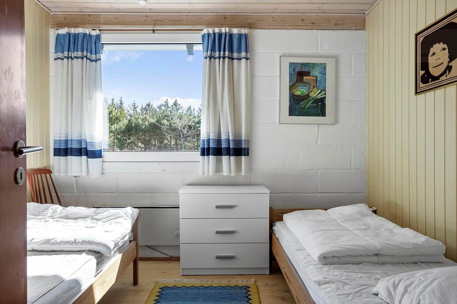 Zimmer mit zwei Betten, Fenster, Gardinen und Schrank.