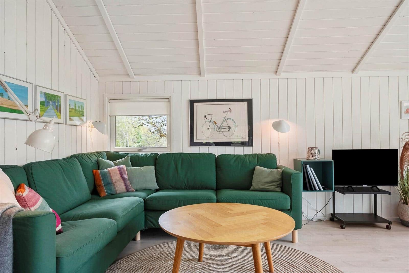Ein Wohnzimmer mit grünem Sofa, runden Tisch und Wandbildern.
