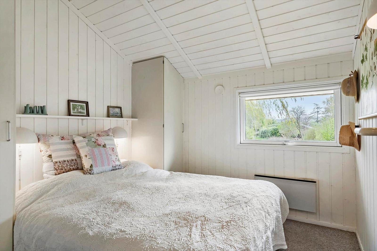 Schlafzimmer mit Bett, Fenster und weißen Wänden.