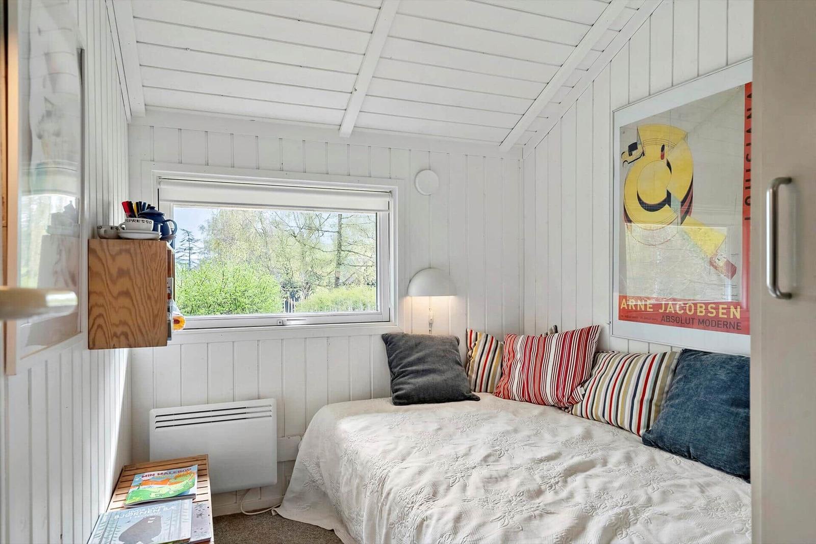 Schlafzimmer mit weißem Holzpaneelen, Fenster und Bett mit Kissen.