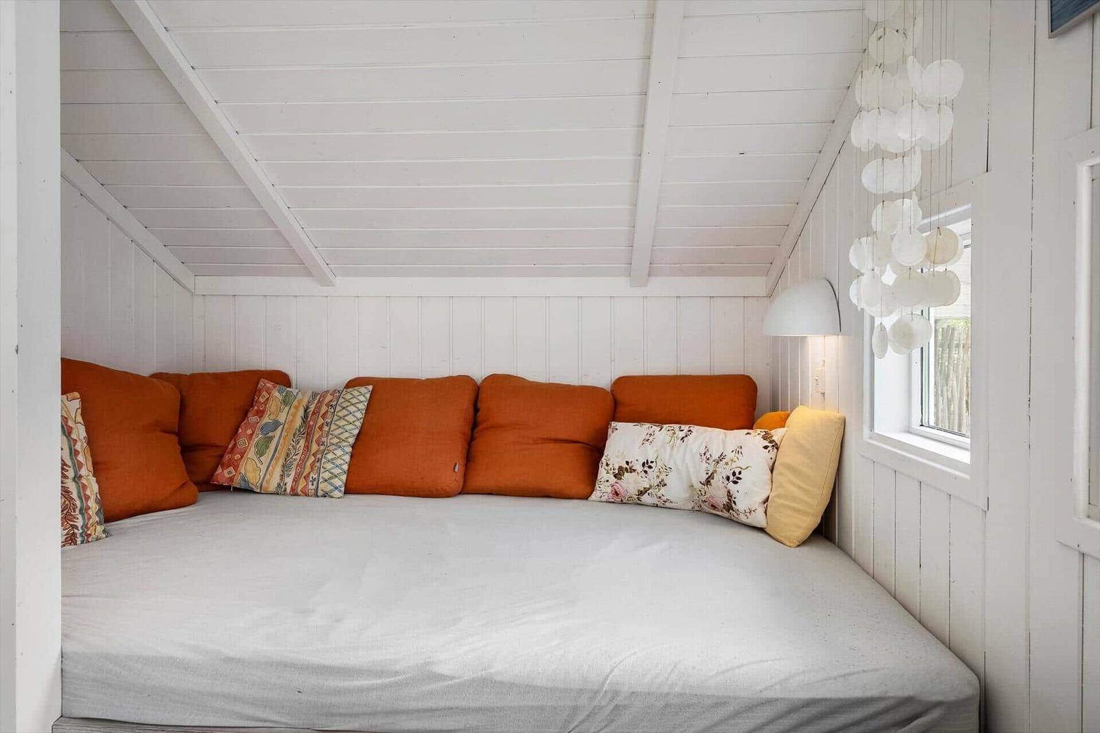 Ein Sofa mit orangefarbenen Kissen und gemusterten Kissen in einem Raum mit weißem Holzverkleidung.